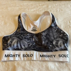 Svartvit träningsväst Mighty Solo plus tillhörande tights - Säljer en sportig svartvit träningsväst från Mighty Solo med tropiskt bladmönster. Västen har bred resår med logga, brottarrygg och är tillverkad i stretchigt material av polyester och spandex. Perfekt för dig som vill ha en snygg och bekväm look på gymmet.Plus tillhörande tights
