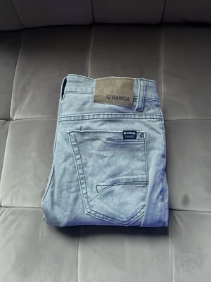Ljusgrå jeans från Garcia - Säljer ett par ljusgrå jeans från Garcia med klassisk femficksdesign och raka ben. Jeansen har en snygg tvättad look och patch med Garcia-logga bak i midjan. Perfekta till en avslappnad stil och passar till det mesta.