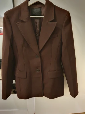 Brun peplum kavaj från Zara  - Stilren brun hourglass/peplum kavaj från Zara med två knappar framtill och klassisk krage. Kavajen har långa ärmar, två fickor med lock och markerad midja för en snygg siluett. Perfekt för dig som vill ha en tidlös och trendig look. (Kavajen är lite trasig inuti efter tvätt! Men inget som syns när den är på eller man stör sig på)