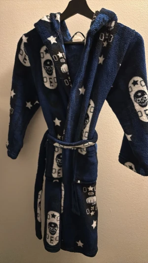 Marinblå morgonrock med döskallar barn 134/140 - Mysig marinblå morgonrock med huva och bälte i midjan. Microfleece