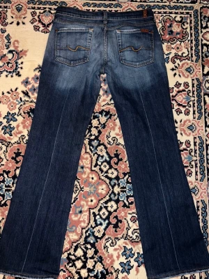 Blå bootcut jeans från 7 For All Mankind - Säljer ett par klassiska blå jeans från 7 For All Mankind med bootcut passform. Midjemått 38cm och Innerbenslängden 75cm💕