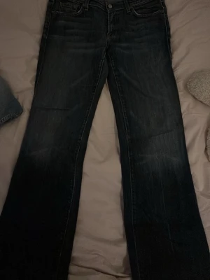 Mörkblå bootcut jeans från 7 for all mankind - Snygga mörkblå jeans från 7 fot all mankind med klassisk femficksmodell och bootcut passform. Jeansen har en rak midja och är tillverkade i slitstarkt denimtyg. Perfekta för dig som gillar en tidlös och avslappnad stil.
