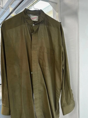 Olivgrön henley från Reliant - Olivgrön henley-skjorta från Reliant med ståkrage och knappar framtill. Skjortan har en bröstficka och är tillverkad i en mix av polyester och bomull. Långärmad och loose fit för en chill vibe.