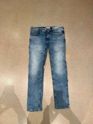 Blå Replay anbass jeans - Säljer ett par klassiska blå jeans från Replay anbass och snyggt slitna detaljer. Jeansen har fem fickor, normal midja och är tillverkade i mjukt bomullsdenim. Perfekta för en avslappnad och trendig look. Använda 2-3 ggr.