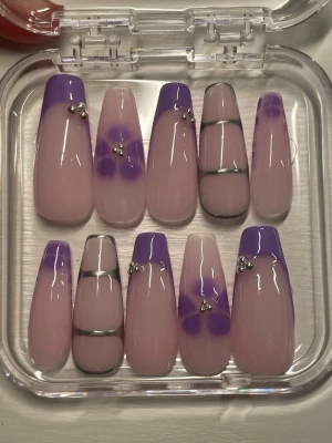 Lila och silver dekorerade lösnaglar - Säljer ett set med långa lösnaglar.designade i ljusrosa bas med lila fransk tipp, blommönster och silverdetaljer. Du får med en genomskinlig ask som du kan förvara dom i när du inte har på dig dom. Se exact storlek på sista bilden