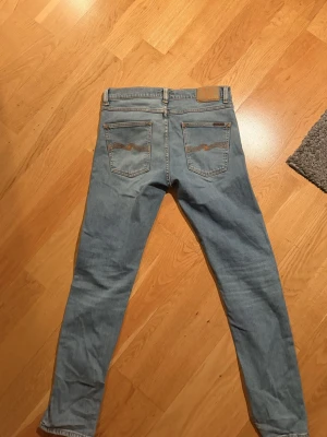 Ljusblå  jeans från Nudie - Säljer ett par ljusblå  jeans från Nudie med klassiska bakfickor och orangea sömmar. Lean Dean 30:32