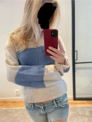 Randig stickad tröja i blått och vitt - Säljer en mysig stickad tröja med breda ränder i ljusblått och vitt. Tröjan har en relaxed passform, rund hals och långa ärmar. Från KIABI storlek S, superbra skick. 