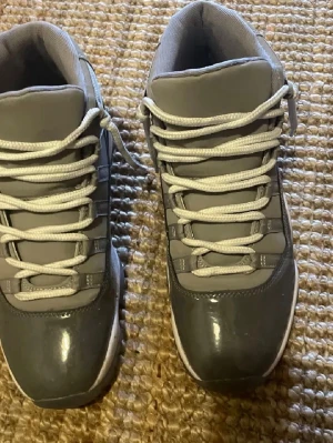 Nike Air Jordan 11 Cool Grey sneakers - Snygga Nike Air Jordan 11 Cool Grey sneakers med högt skaft. Skorna har en grå ovandel i både mocka och lackat material, vita snören och en vit sula. Perfekta för dig som gillar klassiska och stilrena sneakers med ikonisk design.