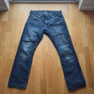 Levi's 501 blå jeans straight fit - Klassiska blå Levi's 501 jeans med rak passform och fem fickor. Jeansen har en mörk tvätt med snygga slitningar och är tillverkade i robust bomullsdenim. Perfekta för en avslappnad och tidlös look.