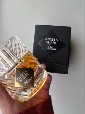 Kilian Angels' Share parfym - Exklusiv parfym från Kilian, Angels' Share, i en lyxig genomskinlig glasflaska med guldfärgad vätska. Flaskan har ett elegant, kristallin mönster och svart etikett. Levereras med svart, stilren förpackning. 
