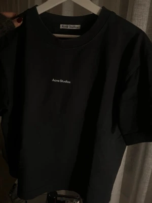 Svart Acne Studios t-shirt - Snygg svart t-shirt från Acne Studios med minimalistisk logga tryckt på bröstet. Klassisk rund halsringning och korta ärmar. Perfekt basplagg för en clean och stilren look.