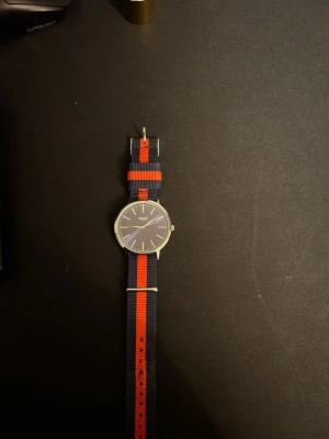 Marine blå regal klocka - Bilderna visar en klocka med marinblå och röd randigt tygarmband från Regal, 