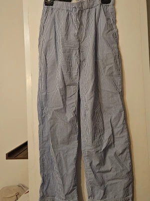 Randiga pyjamasbyxor från ARKET - Snygga pyjamasbyxor från ARKET i blåvitt randigt mönster. Byxorna har rak passform, resår i midjan och är tillverkade i ett mjukt och lätt tyg som känns skönt mot huden. Perfekta för mysiga sommarmorgnar! Omsydda i rumpan av mig för bättre passform.