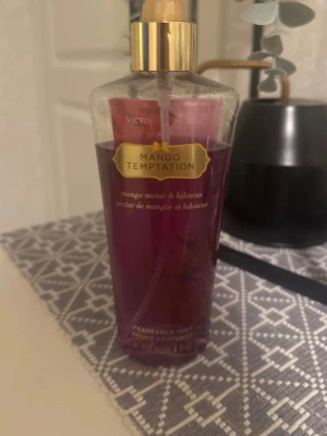 Victoria's Secret Mango Temptation mist - Fräsch body mist från Victoria's Secret i doften Mango Temptation. Flaskan är genomskinlig med guldigt lock och innehåller en lila-rosa vätska. Doften har inslag av mango och hibiskus, perfekt för dig som gillar fruktiga och blommiga toner. Lite är använt