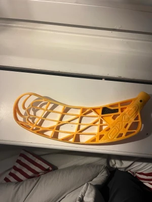 Orange innebandyblad OXDOG AVOX - Säljer ett orange innebandyblad i plast med öppet rutmönster och lätt böjd form. Bladet har en svart detalj nära fästet och passar till de flesta innebandyklubbor. Perfekt för dig som vill byta blad på klubban och få bättre bollkontroll.