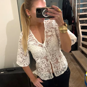 Vit spetsblus från NA-KD - Superfin vit blus från NA-KD med v-ringning och halvtransparent spetsmaterial. Blusen har trekvartsärmar och knappar framtill. Detaljerad spets med blommönster ger en romantisk vibe. Säljer då jag råkade beställa hem 2 och missa att skicka tbx, köpt för 599🩷