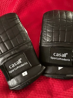 Svarta boxningshandskar från Casall L  - Säljer ett par svarta boxningshandskar från Casall Sports Products. Handskarna är tillverkade i vadderat konstläder med vit insida och svart utsida. De har breda kardborreband för extra stöd och ventilation på handflatan. Perfekta för träning eller sparring.