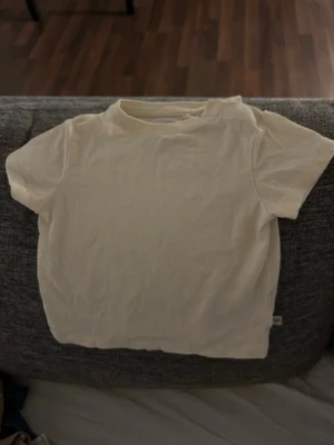 Bebis kläder Vit kortärmad t-shirt  - En basic vit t-shirt från lager 157 i mjuk bomull, perfekt för små barn. Klassisk rund halsringning och korta ärmar. Enkel och stilren design utan mönster eller tryck, lätt att matcha med allt.