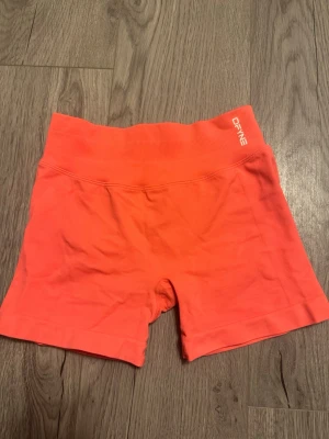 Korta korall träningsshorts från DFYNE - Snygga och stretchiga korall färgade shorts från DFYNE med hög midja och ribbad linning. Perfekta för träning och har en tight passform. Finns inte att köpa längre storlek xs köpta på vinted, de är mer korall färgade än orangea 