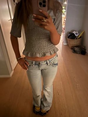 Grå t-shirt från H&M  - Säljer en grå smockad  t-shirt från H&M Divided i storlek XS. T-shirten har korta ärmar, smockad midja och volangkant nedtill. Knappt andvänd men säljer för tröjan inte passar mig!💓💗