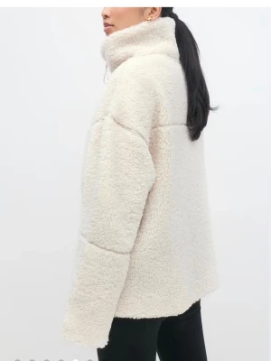 Beige teddyjacka från Gina Tricot - Supermjuk och fluffig teddyjacka i beige från Gina Tricot. Jackan har hög krage, dragkedja framtill och en loose passform. Perfekt för kyliga dagar när du vill vara både varm och snygg.