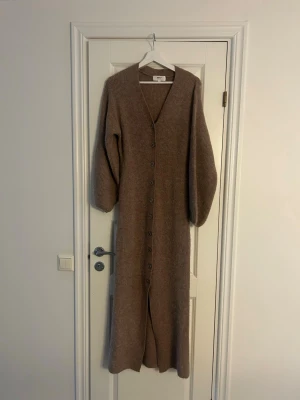 Lång beige stickad kofta Gina Tricot - Lång, beige stickad kofta från Gina Tricot med v-ringning och knappar hela vägen ner. Koftan har långa, lite pösiga ärmar och är gjord i ett mjukt, ribbstickat material. Perfekt för lager på lager och en chill look.