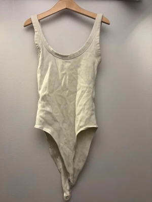 Beige ribbad body  - En enkel och stilren beige body med breda axelband och rundad urringning. Tillverkad i ett mjukt, ribbat material som ger en bekväm passform. Knäppning i grenen för enkel på- och avtagning. Perfekt att styla med jeans eller kjol. För vardagsammanhang eller om man vill klä upp sig! Använd ett till två gånger och därför mycket bra skick!