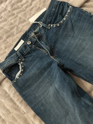 Blå jeans med nitar från zara - Snygga blå jeans från Zara med coola nitar längs fickorna och benen Klassisk femficksmodell med dragkedja och knapp. Jeansen har en rak passform och är gjorda i denim med lätt tvättad look. Perfekta för dig som vill ha jättebekväma jeans som sticker ut lite. Är storlek 38men passade inte mig som vanligtvis har 38-40 så mer åt s/m hållet. Helt slutsålda! Nypris 559 kr.