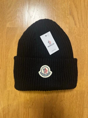Svart  Moncler mössa - Snygg svart ribbstickad mössa från Moncler. Ett måste nu under kalla dagarna! 