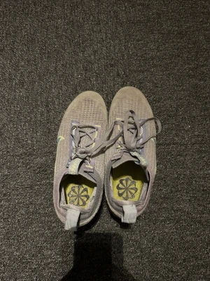 Nike grå/lila Air Vapormax sneakers - Nike Air Vapormax sneakers i grått och lila meshmaterial med genomskinlig sula och turkos Swoosh på sidan. Skorna har snörning, dragflik bak och en unik blomdetalj på innersulan. Perfekta för dig som gillar sportig och modern stil.