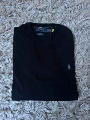 Svart tröja från Polo Ralph Lauren - Klassisk svart tröja från Polo Ralph Lauren med rund halsringning och diskret broderad logga på bröstet. Slim fit passform och helt oanvänd, storlek S.