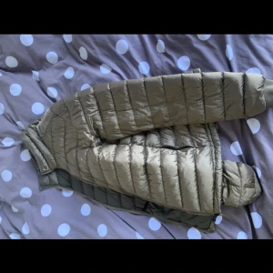 Ljusbrun dunjacka från Gang - Snygg ljusbrun dunjacka med klassisk quiltad design och ståkrage. Jackan har en smal passform och horisontella sömmar som ger en modern look. Perfekt för kalla vinterdagar och enkel att matcha med olika outfits. Köpte den förra vintern men fick fel storlek så har inte kommit till användning!