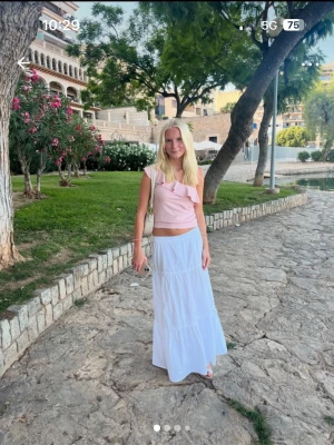 Ljusrosa volangtopp med asymmetrisk axel - Säljer en ljusrosa topp med volangdetalj och asymmetrisk axel. Toppen är ärmlös och har en ribbad struktur som ger en snygg och modern look. Perfekt för varma dagar och enkel att styla med kjol eller jeans.