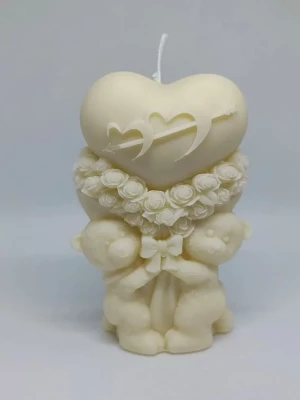 Dekorativ ljus med nallebjörnar och hjärta - Säljer ett krämvitt dekorljus i form av två nallebjörnar som håller ett stort hjärta med ingraverade hjärtan och pil. Ljusets mitt är dekorerat med rosor och en rosett. Perfekt som present eller inredningsdetalj.