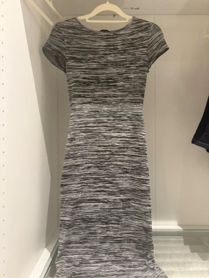 Gråmelerad  klänning - Klänning i gråmelerat mönster med rund halsringning och korta ärmar. Klänningen har en enkel, figurnära passform och är tillverkad i ett mjukt material som känns bekvämt mot huden. 