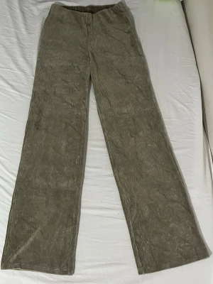 Olivgröna vida manchesterbyxor - Säljer ett par helt oanvända olivgröna manchesterbyxor med raka, vida ben och hög midja. Byxorna har klassisk bredspårig manchesterstruktur och är perfekta för dig som gillar stiliga och sköna material. Inga synliga fickor. Passar till många olika looks!