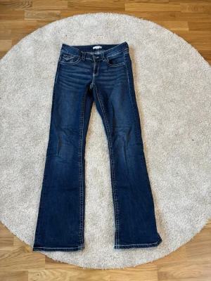 Mörkblå bootcut jeans - Snygga mörkblå bootcut jeans med klassisk femficksdesign och kontrastsömmar. Jeansen har låg midja och utsvängda ben, perfekta för en avslappnad och trendig look. Tillverkade i denim med lätt stretch för extra komfort.