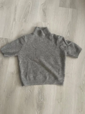 Grå stickad tröja med polokrage - Mysig grå stickad tröja med korta ärmar och polokrage. Tröjan har en rak passform och ribbstickade, passar S och M lika bra.