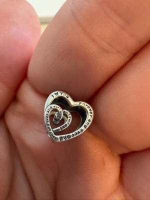 Pandora hjärtberlock i silver - Säljer en snygg Pandora berlock i form av ett öppet hjärta i silver. Texten 'I love you forever and ever and ever' är ingraverad i en spiral runt hela berlocken. Perfekt att hänga på ett armband för en personlig touch.
