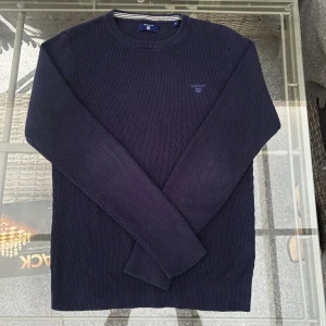 Stickad GANT-tröja S - Mörkblå stickad tröja från GANT i storlek S, perfekt för dig som gillar klassisk och stilren design. Tröjan har en strukturstickad yta i mjukt bomullsmaterial, vilket gör den både bekväm och hållbar. Passar utmärkt till både jeans och chinos – lika fin till vardag som till lite finare tillfällen. I mycket bra skick, knappt använd!  Storlek: S (normal i storleken) Färg: Mörkblå / navy Material: Bomull Skick: Mycket bra  ✨ En tidlös GANT-tröja som lyfter varje outfit – perfekt basplagg till hösten