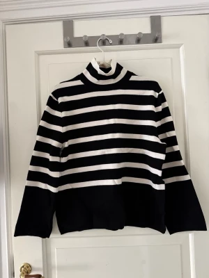 Randig tröja  - Randig tröja med hög krage. Vit och svart. Från H&M i storlek XS men passar även S. Lite styvare material. Använd ett fåtal gånger. Slits på sidorna. 
