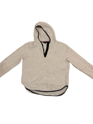 Vit stickad hoodie med svarta detaljer - Mysig vit stickad hoodie med svarta kanter vid huva, ärmslut och nederkant. Tröjan har lång ärm och en djup v-ringning framtill. Perfekt för lager-på-lager och chill dagar.