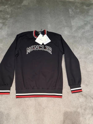 Svart Moncler sweatshirt  - Nu säljer jag min sjukt feta moncler sweatshirt. Den är stilren och passar till allt! Den är nästan helt oanvänd (använd 3 gånger). Det kan vara en A kòPï@, men är den det så är den sjuk bra för den ser äkta ut (men ingen garanti då inte jag har köpt den). Storlek L passar M. Tveka inte på att höra av dig vid några frågor så svarar jag snabbt! 