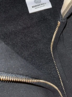 Svart zip hoodie från Burberry - Snygg svart hoodie från Burberry med dragkedja framtill, justerbar huva med snören och klassisk känguruficka. Tillverkad i mjukt material som känns lyxigt och bekvämt. Perfekt för dig som vill ha en stilren och exklusiv look.