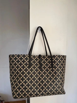 By Malene Birger Abigail väska  - Säljer min så söta väska från by Malene Birger. Den är i väldigt bra skick, däremot har ena handtaget blivit lite slitet vilket är väldigt vanligt på denna modellen. Den har lite fläckar på insidan men inget man tänker på om den har saker inuti. Den är créme vit och svart med det klassiska Marlene Birger mönstret och har brunt tyg på insidan. Verkligen så fin väska perfekt för skolan eller jobbet om man ska ha en dator eller liknande. 💗