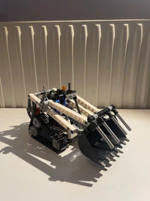 LEGO Technic Bandlastare 42032 - Säljer en LEGO Technic bandlastare modell 42032. Byggsatsen är svart, vit och grå med detaljer i orange och blått. Modellen har rörliga band, skopa och häftig mekanik. Perfekt för dig som gillar teknik och byggleksaker.