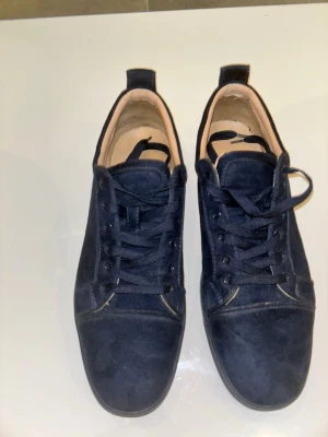 Mörkblå loubs med snörning - Stilrena sneakers i mörkblå mocka med klassisk låg profil och matchande mörkblå skosnören. Skorna har en enkel design med ljus insida och diskreta sömmar. Perfekta för dig som gillar en clean och tidlös look.