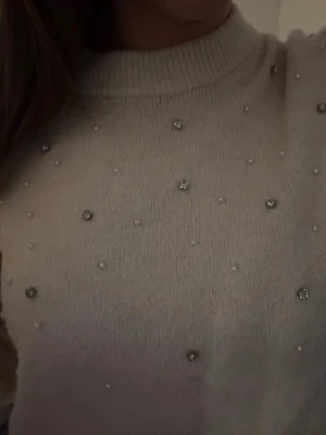 Beige stickad tröja med pärlor - Säljer en beige stickad tröja med diamant liknande pärlor både där bak o fram. Säljer för den inte kommer till användning och har nog slutat säljas på H&M