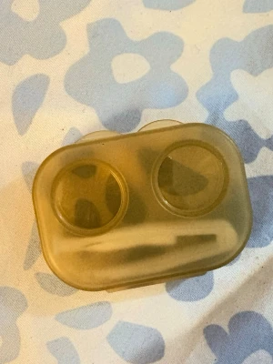 Gul kontaktlinsbehållare i plast - Praktisk gul kontaktlinsbehållare i genomskinlig plast med två fack och lock. Perfekt för att förvara och skydda dina linser när du är på språng. Smidig och kompakt design som enkelt får plats i väskan.