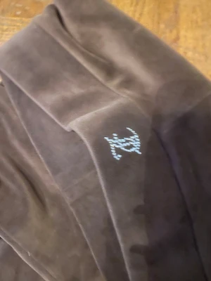 Bruna velourbyxor Juicy Couture XXS - Säljer ett par bruna velourbyxor från Juicy Couture i storlek XXS. Byxorna har bootcut-ben och låg midja, med glittriga strasstenar som bildar texten 'Juicy' på baksidan. Mjukt material och klassisk Juicy-stil, perfekt för dig som gillar Y2K-vibe.